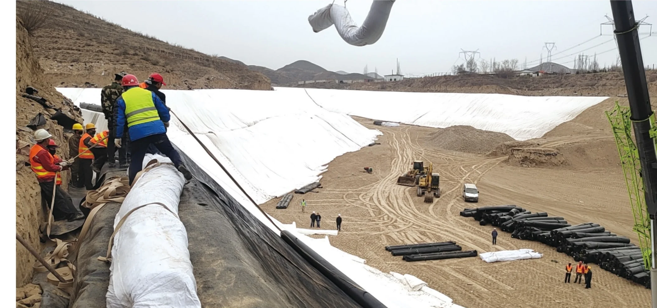 Workers and equipment placing lining materials in a large basin